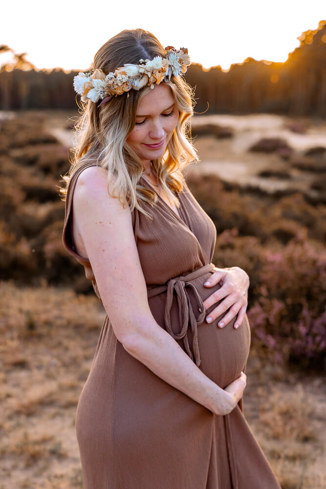 Babybauchshooting im Sonnenuntergang Mama hat ihre Hände am Babybauch, schaut verträumt